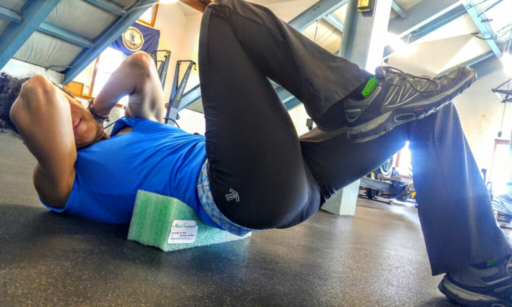 Person exercising with a foam roller under their back in a gym.