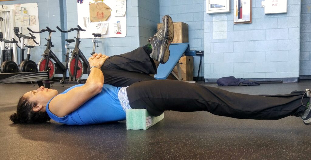 Person stretching hip flexors with a foam block under their back.