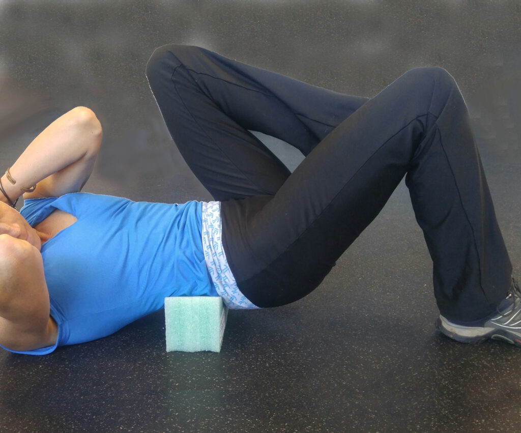 Person lying on back with legs bent, performing an exercise using a foam block.
