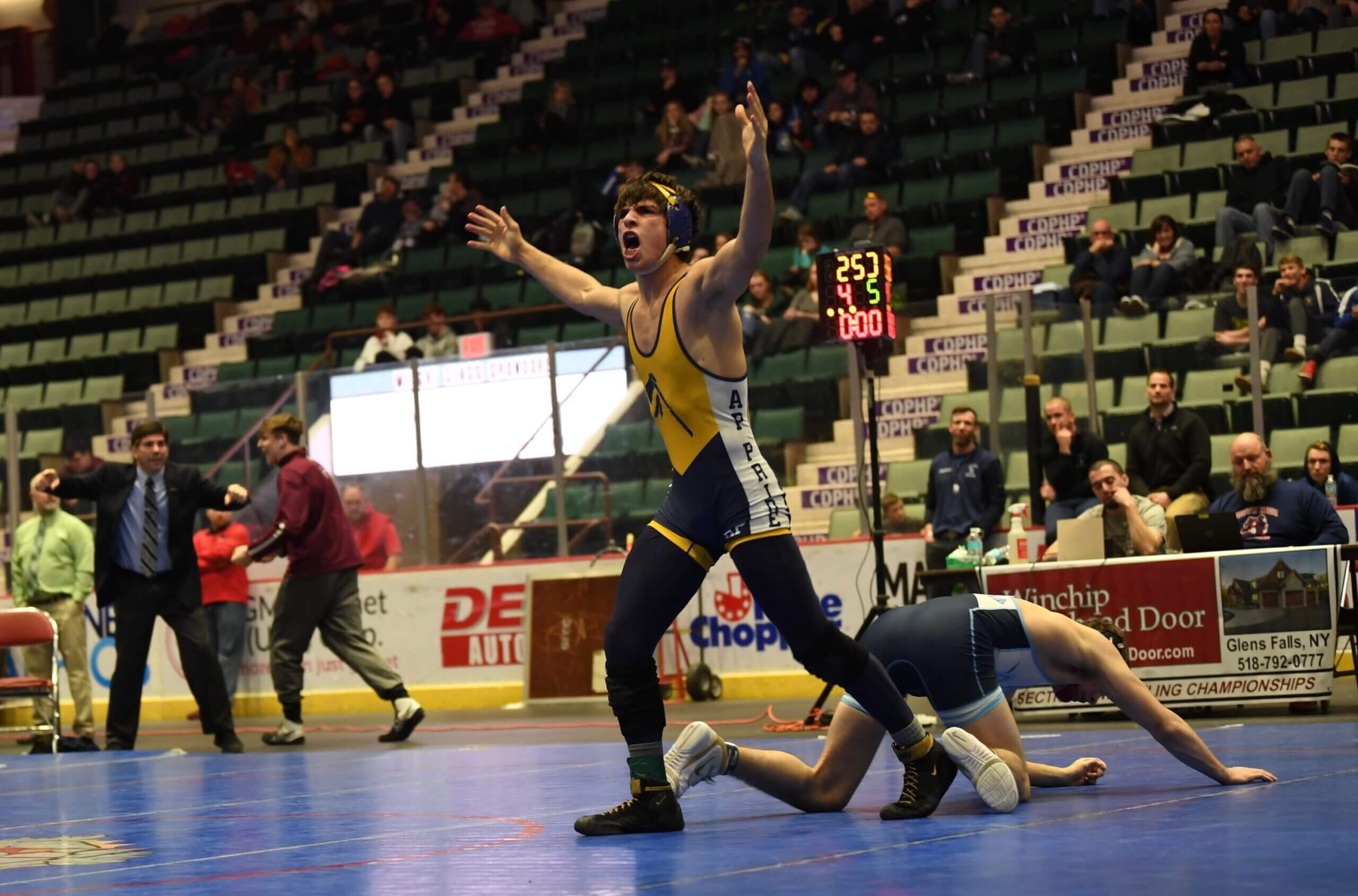 Wrestler celebrates victory while opponent lies on the mat in a crowded arena.